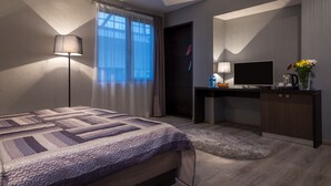 A modern bedroom with a bed, a desk, a TV, and a small coffee table. - Ararat Hotel (Yerevan)