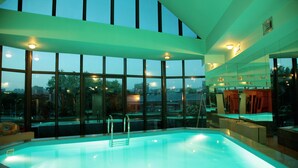 A modern indoor swimming pool with a view of the cityscape through large windows. - Ararat Hotel (Yerevan)