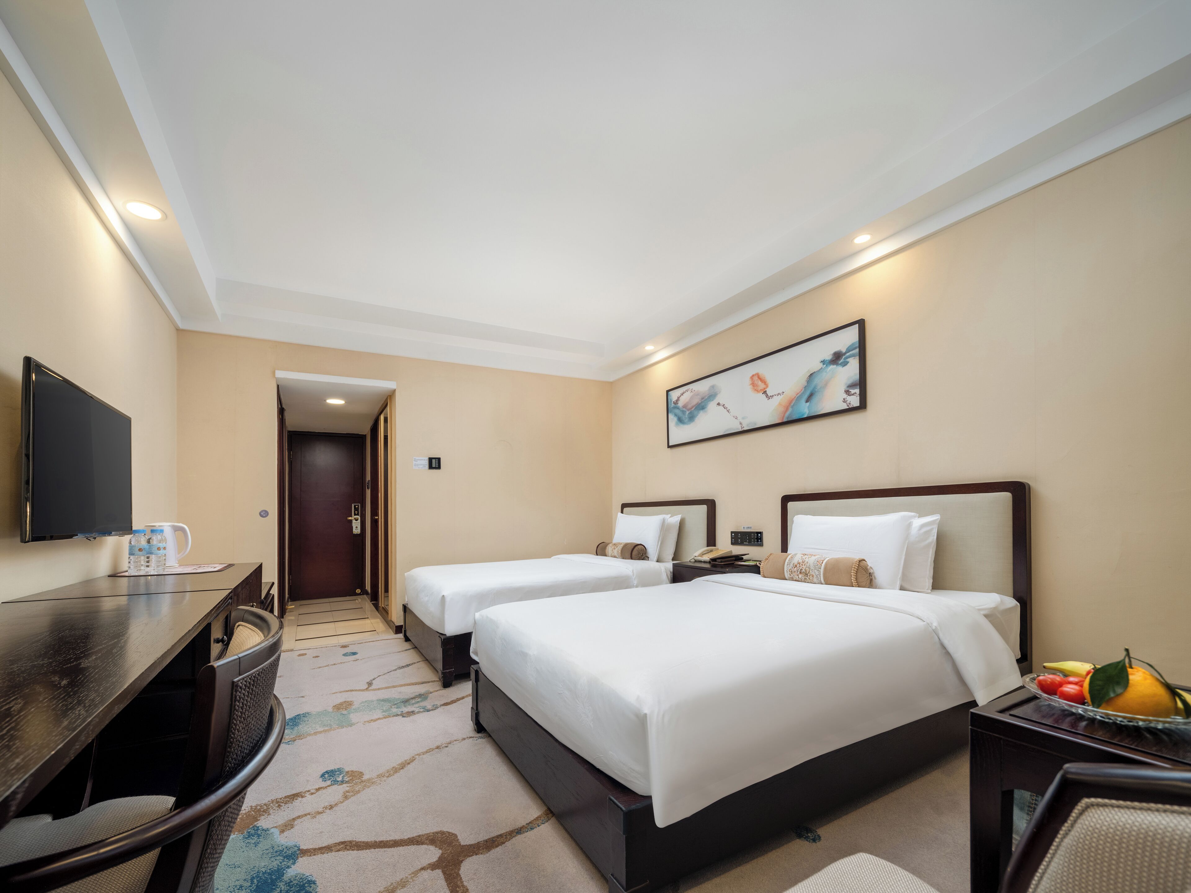 A hotel room with two beds, a desk with a chair, a TV, and a painting on the wall.