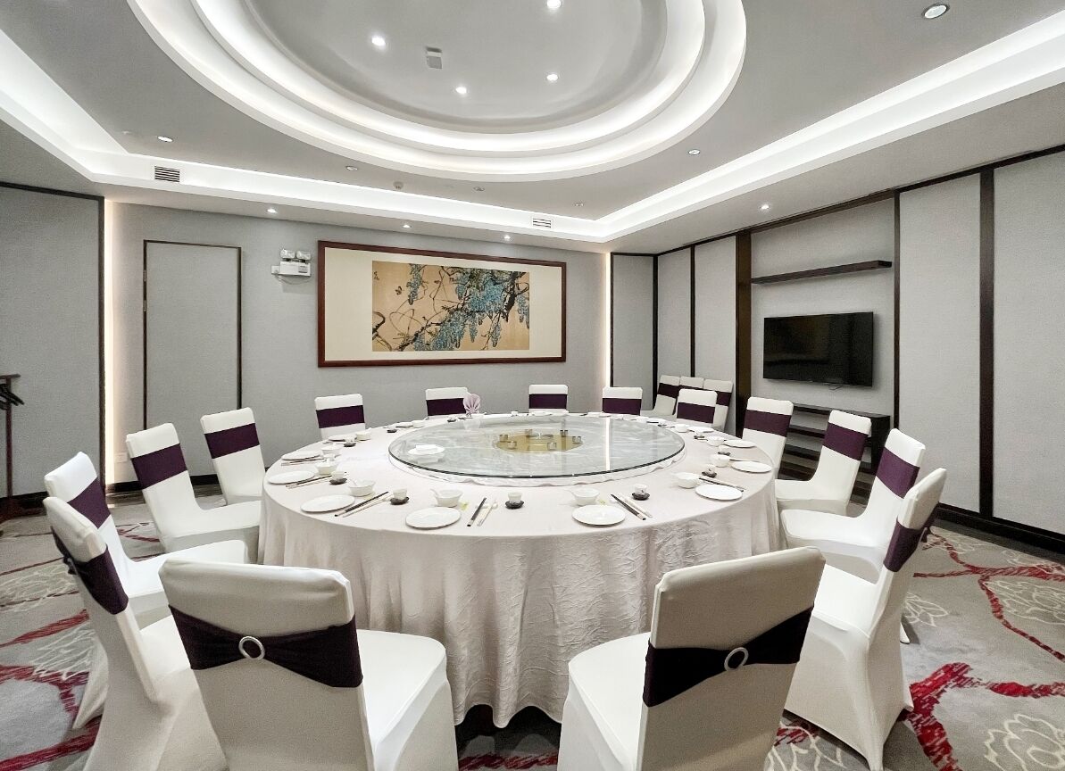 A conference room with a round table, white chairs with purple sashes, a large painting on the wall, and a flat-screen TV.