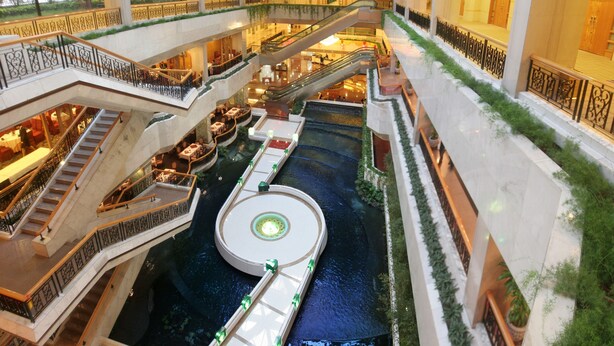 Een meerverdiepings atrium met een centraal waterkunstwerk, diverse trappen en binnentuinen.