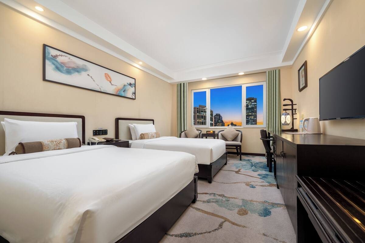 A hotel room with two beds, a desk, a chair, a TV, and a city view.