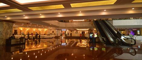 A spacious lobby with a polished floor, a reception desk, and an escalator.