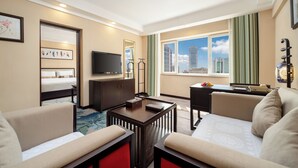 Een hotelkamer met een bed, televisie, bureau en uitzicht op de stad.