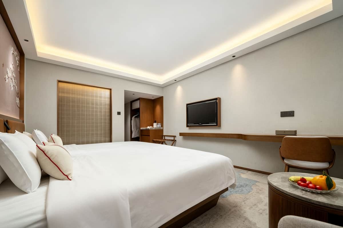 Habitación de hotel moderna con una cama grande, un televisor montado en la pared, un escritorio con una silla y una mesita con fruta.