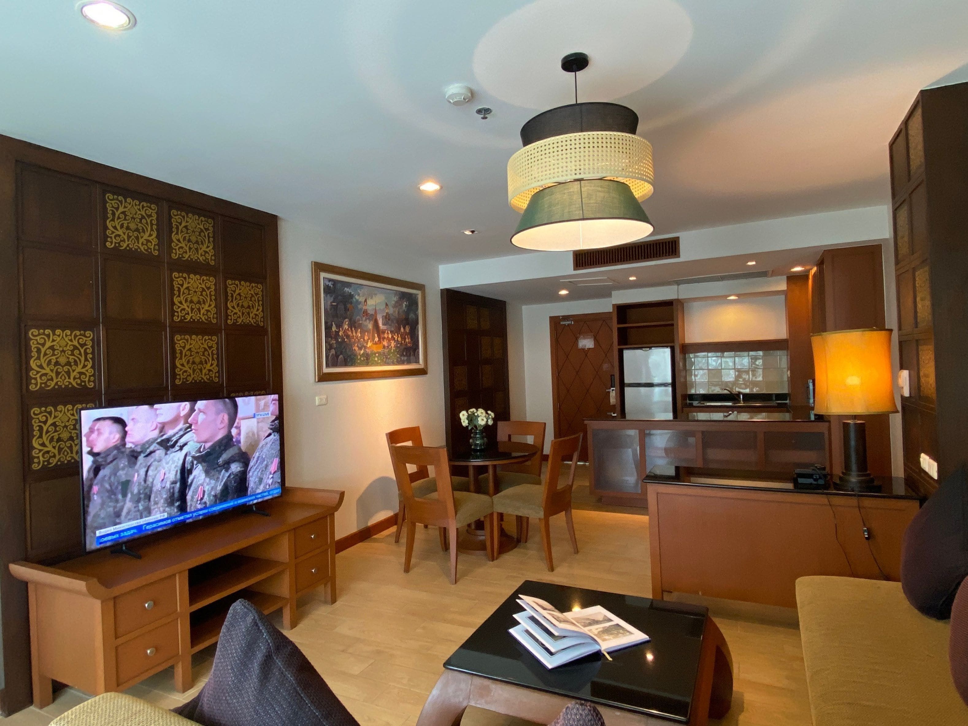 A modern living room with a flat-screen TV, wooden furniture, a dining area, and a kitchen.