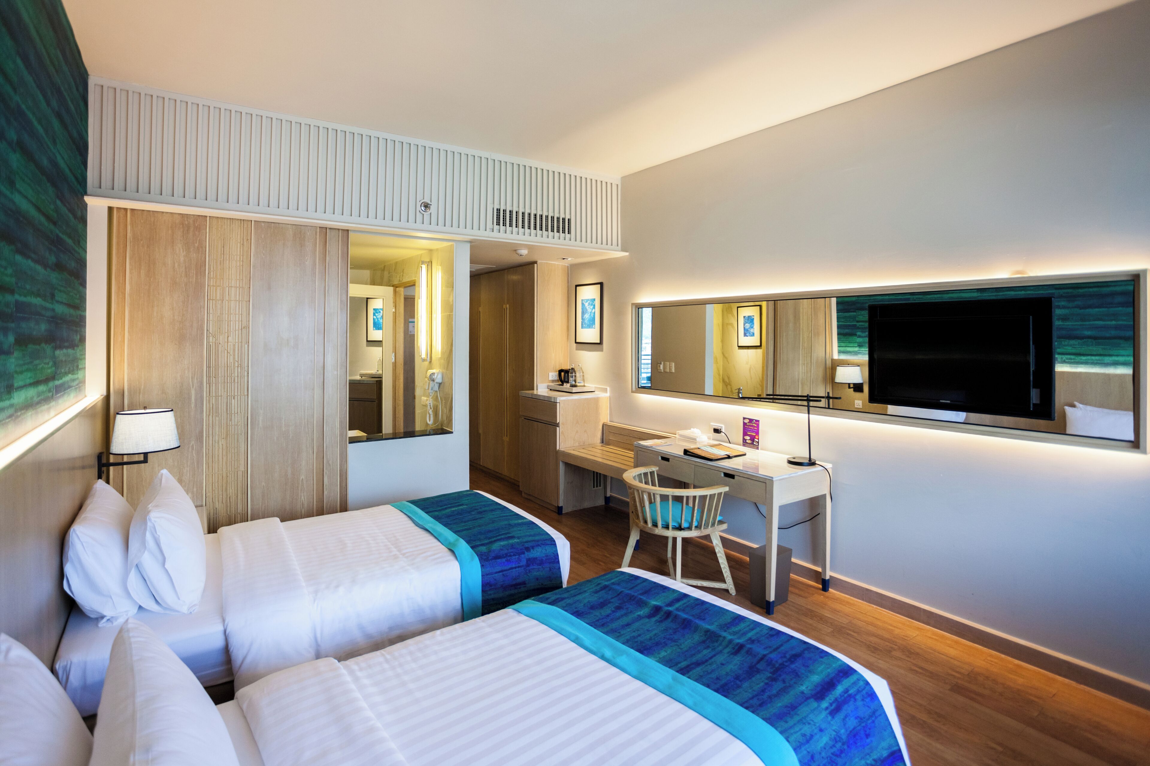 A hotel room with two beds, a desk, a chair, a TV, and a large mirror.
