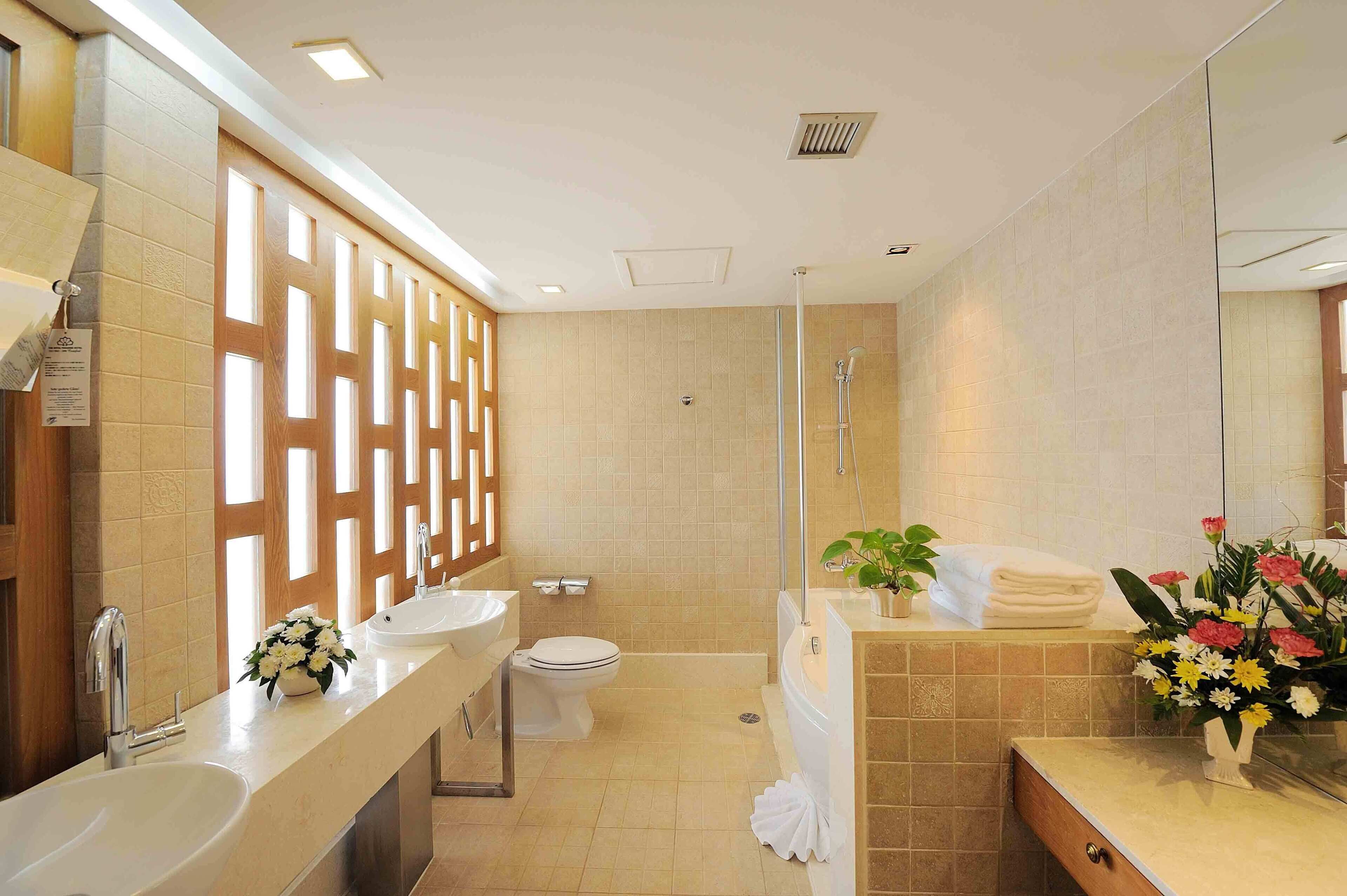 Ein modernes Badezimmer mit einem großen Spiegel, zwei Waschbecken, einer Toilette, einer Dusche und einem Waschtisch mit Handtuchhalter und einer Blumenvase.