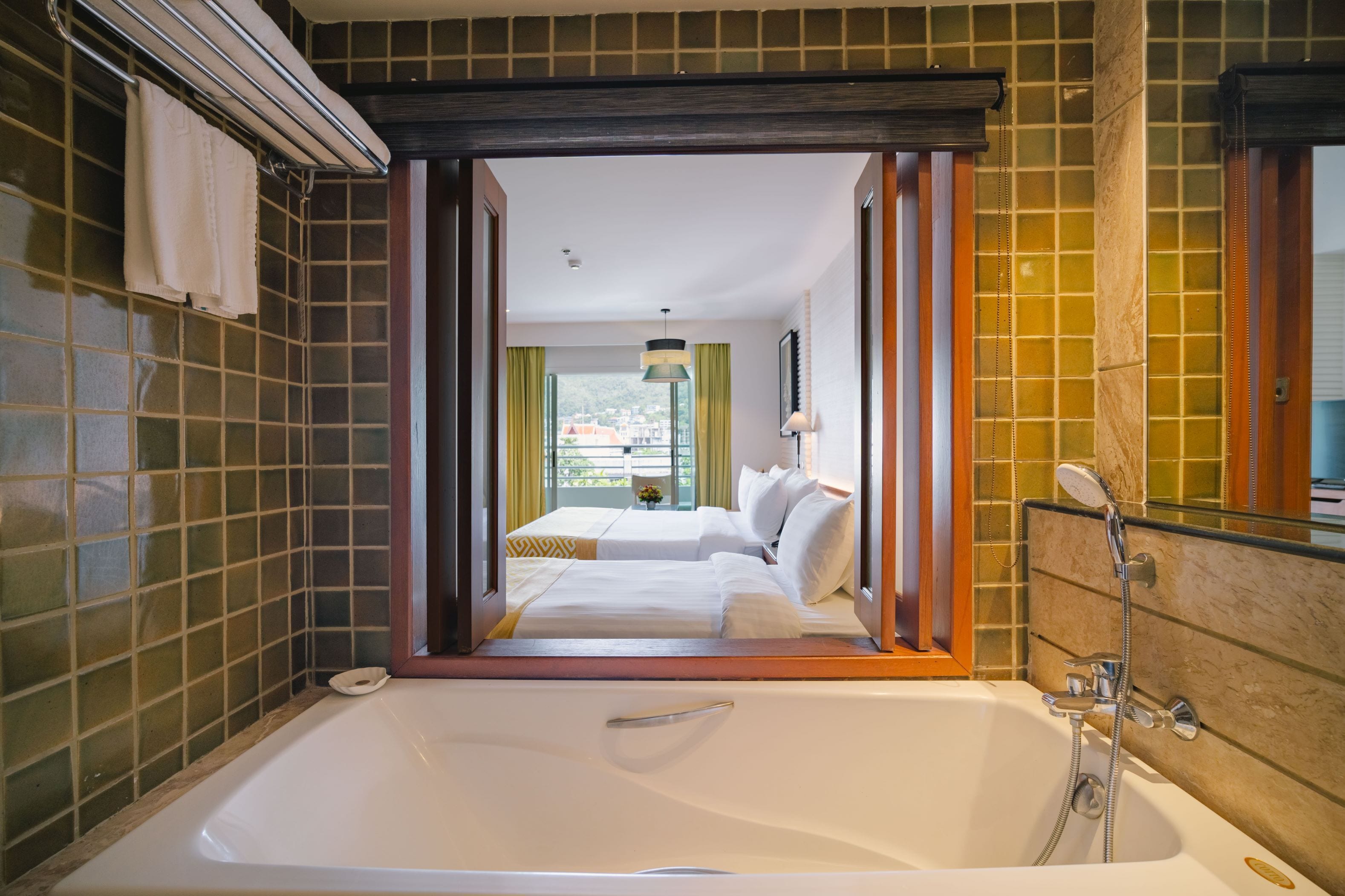 A modern bathroom with a large bathtub, a shower area, and a view of a bedroom with two beds.