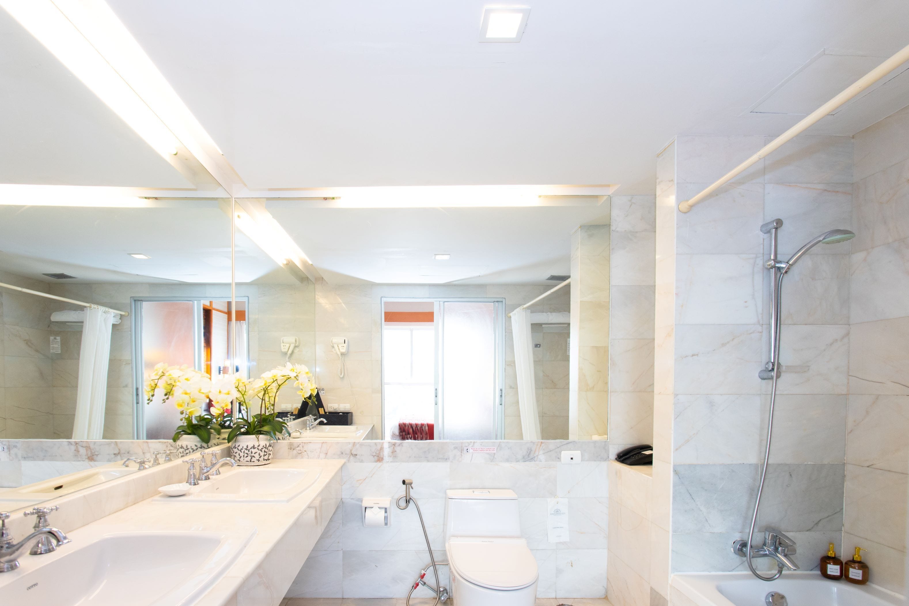 A modern bathroom with a large mirror, two sinks, a toilet, and a shower.