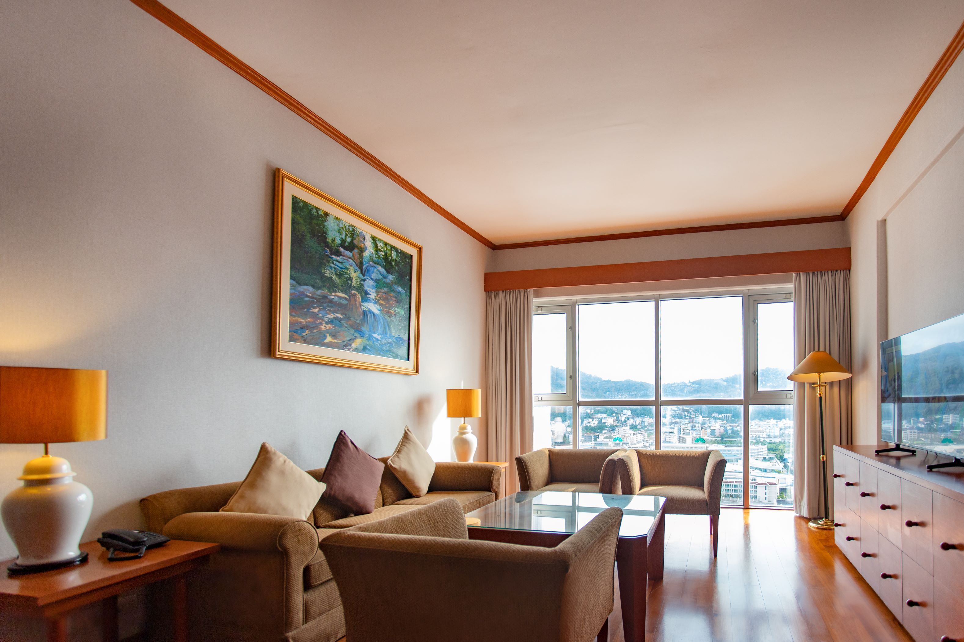 Habitación de hotel con sofá, mesa de comedor, televisor y ventana grande con vista a la ciudad.