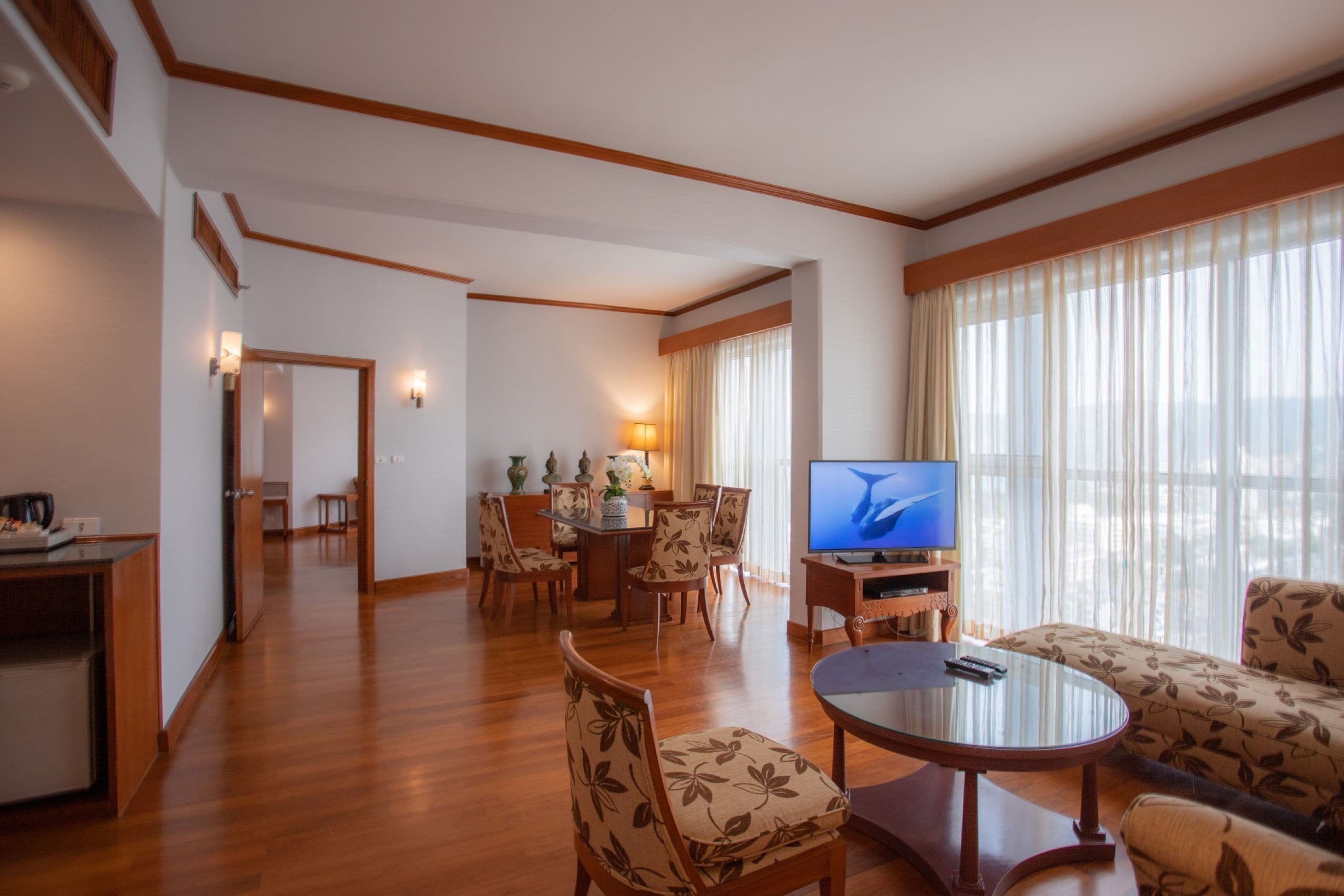 Habitación de hotel con piso de madera, zona de comedor con mesa y sillas, televisor y sofá.