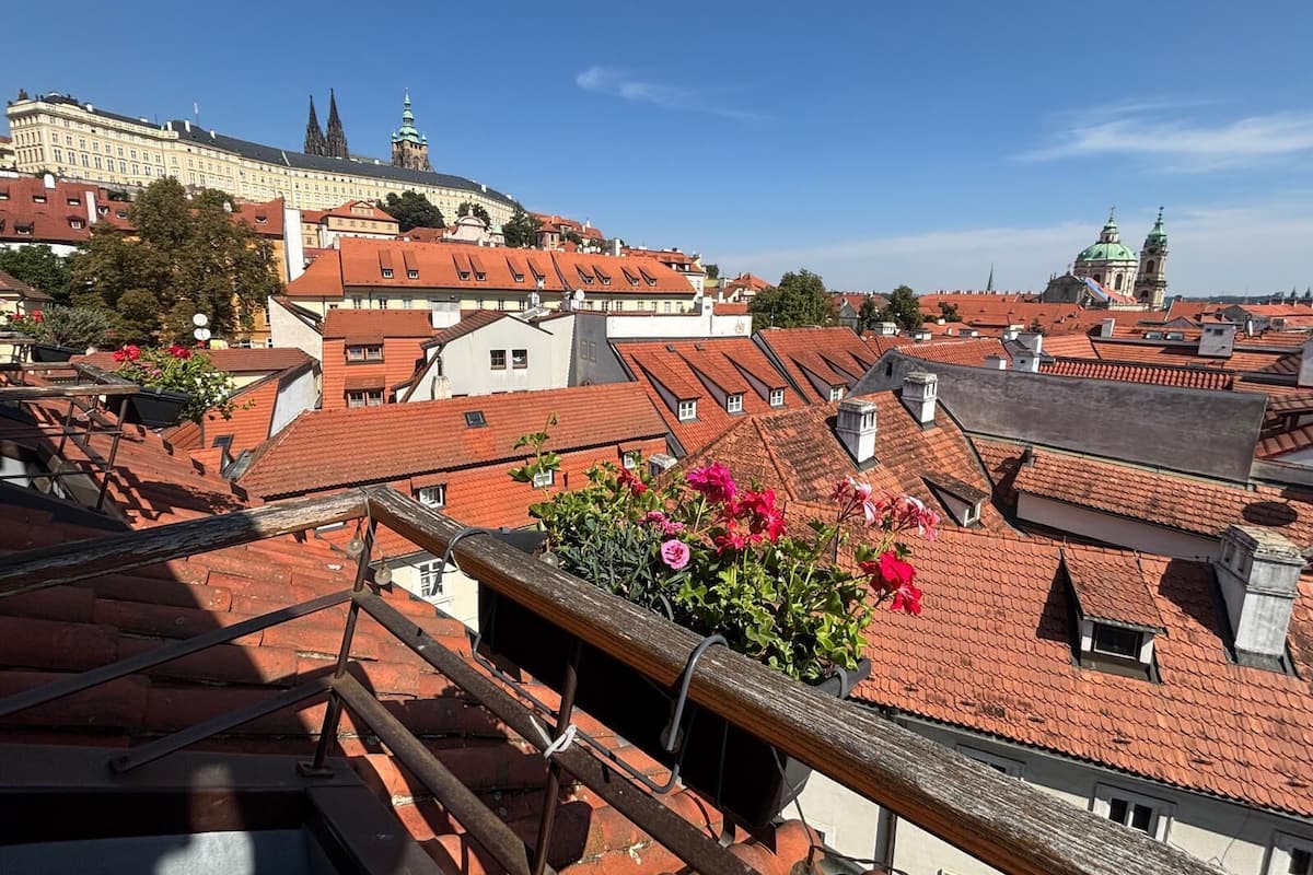 A cityscape with traditional architecture, including a prominent building with a green dome and spires, and a variety of rooftops with red tiles.