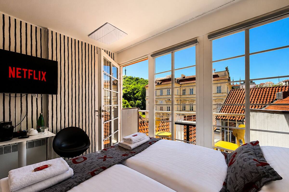 A hotel room with a large window, a bed, a desk with a computer, and a TV displaying 'NETFLIX'.