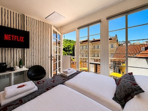 A hotel room with a large window, a bed, a desk with a computer, and a TV displaying 'NETFLIX'. - LH Vintage Design Hotel Sax (Prague)