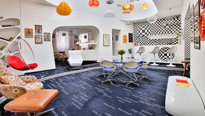A modern hotel lobby with a checkered floor, unique hanging lamps, and a seating area with a red chair and a cushioned bench. - LH Vintage Design Hotel Sax (Prague)