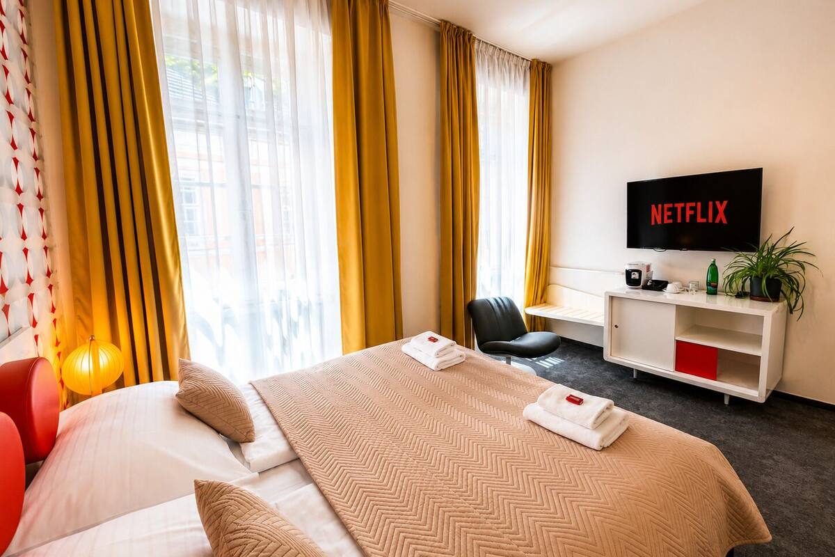 A hotel room with a bed, a desk, a chair, a TV, and a plant.
