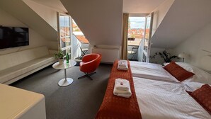 A modern hotel room with a large window, a flat-screen TV, a red chair, two beds with towels, and a ceiling light. - LH Vintage Design Hotel Sax (Prague)