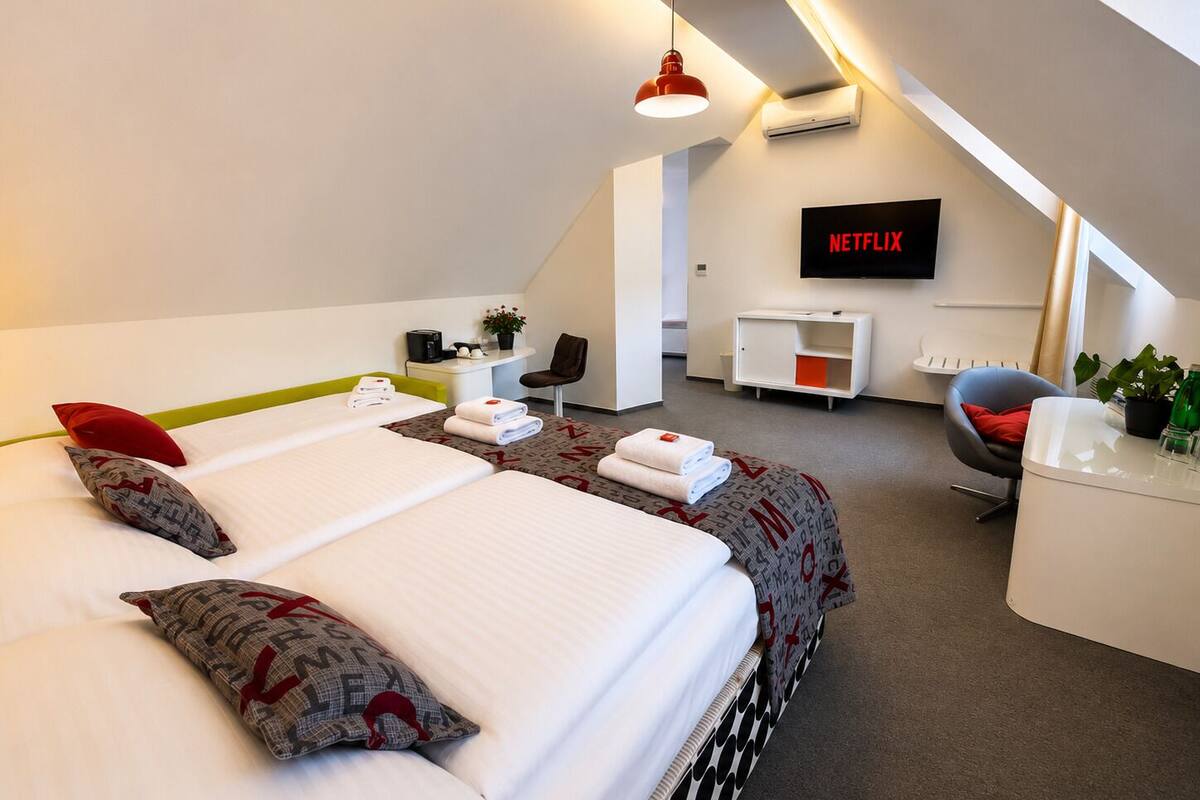 A modern hotel room with a bed, a desk, a chair, a TV, and a small plant.