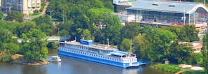 Un barco de paseo atracado en un puerto, con un puente al fondo y un edificio grande de techo curvo.
