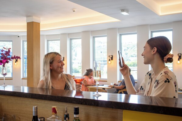 A bar area with a counter, a person holding a smartphone, and another person in the background.