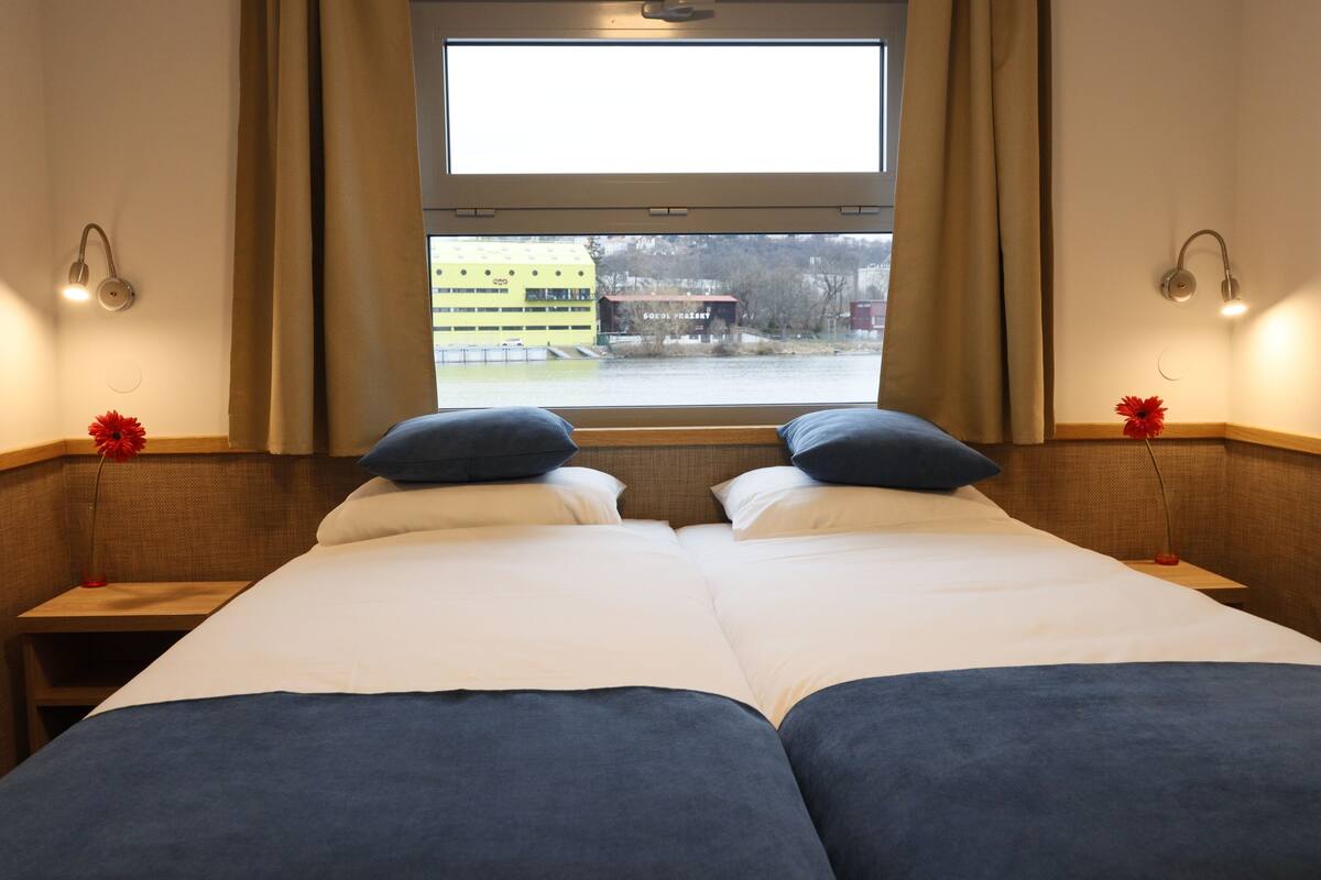 A hotel room with two beds, a large window, and a view of a building outside.