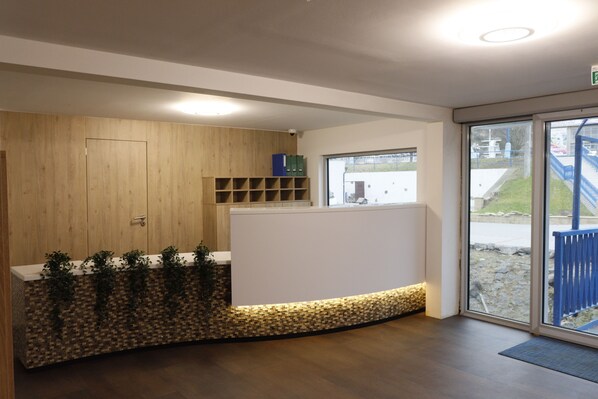 A reception area with a wooden panel wall, a reception desk, a window with a view of the outside, and a blue railing outside. - Botel Racek (Prague)