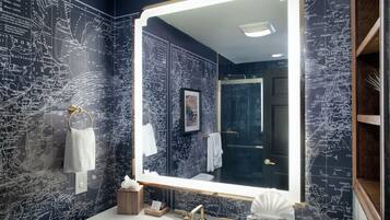 A bathroom with a large mirror, nautical-themed wallpaper, and a white sink with gold fixtures.