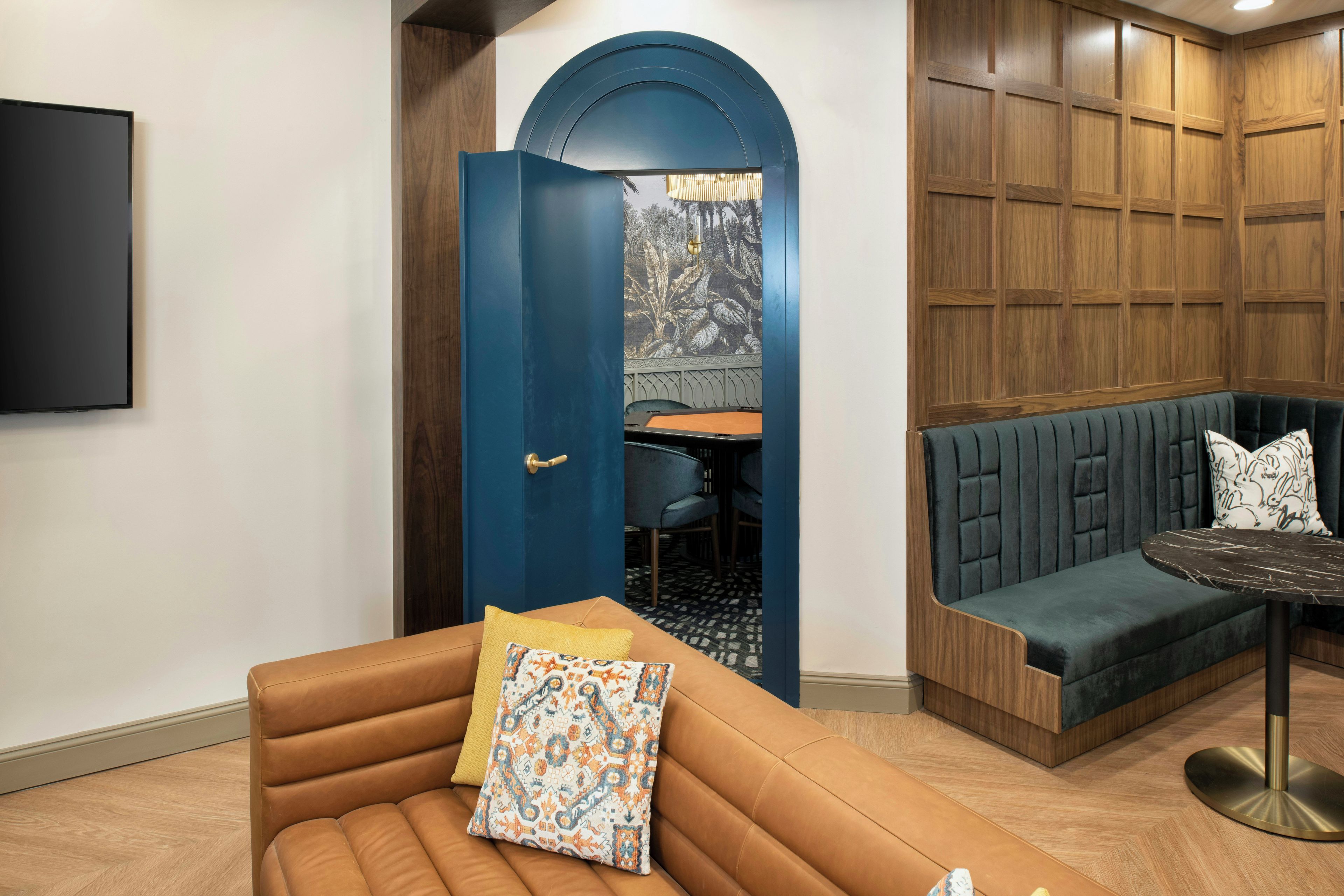 Um interior moderno com um sofá de couro marrom, uma porta azul com painel decorativo e painéis de madeira na parede.