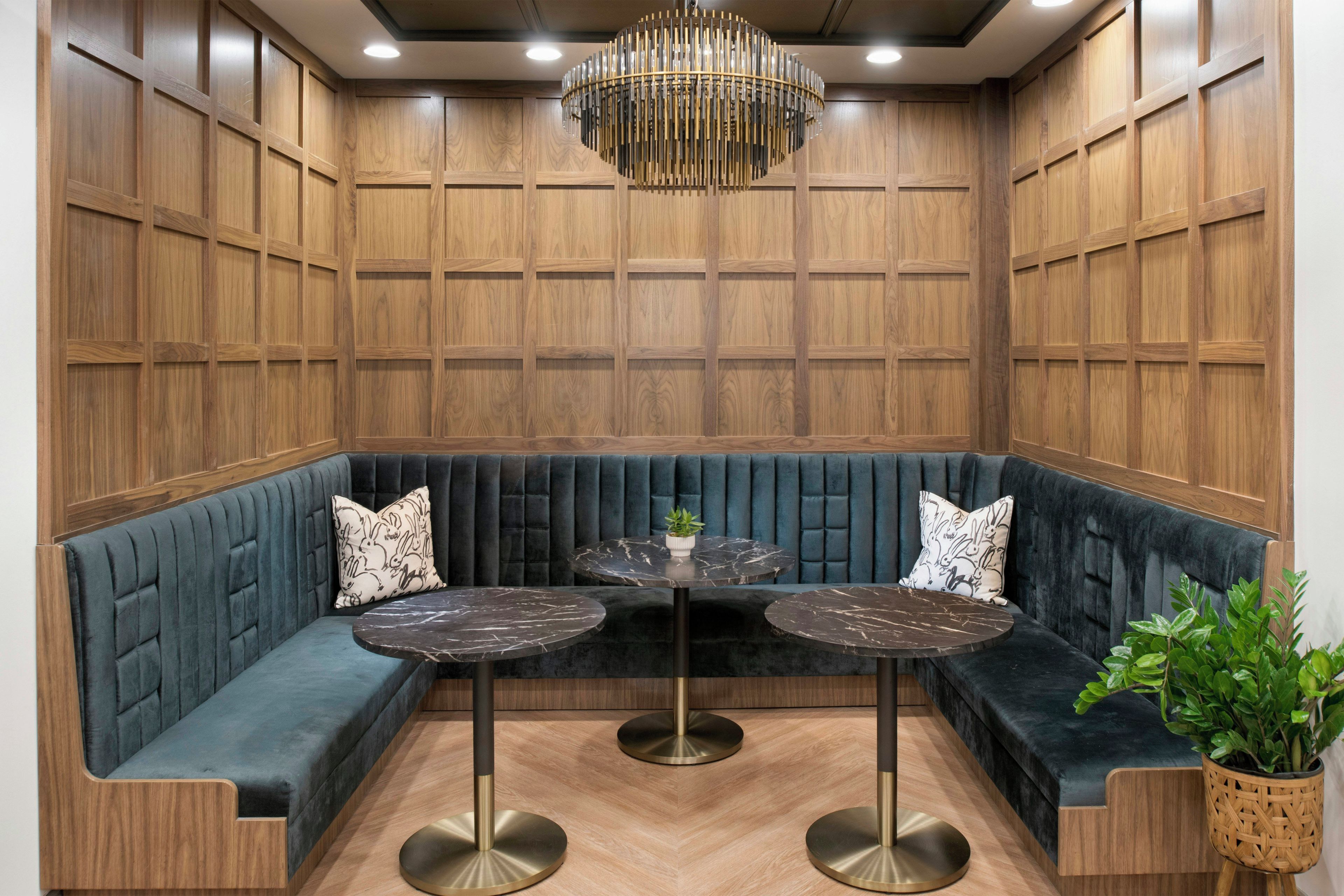 A seating area with a dark blue cushioned bench, two round tables with marble tops, and a decorative chandelier.