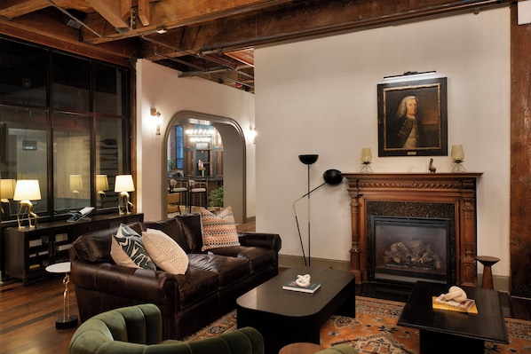 A cozy living room with a leather sofa, a fireplace, and a portrait on the wall. - The Ansonborough (Charleston)
