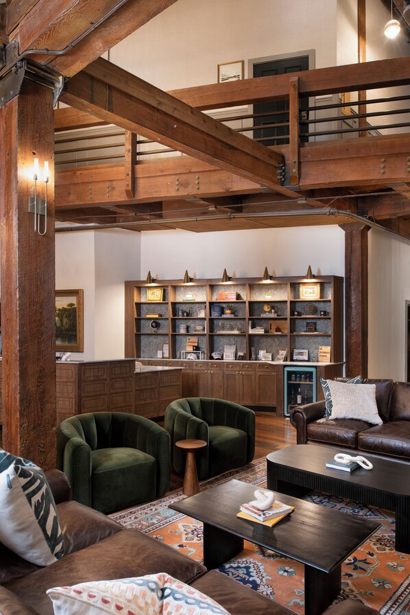 A spacious living area with a high ceiling, wooden beams, a central fireplace, and a cozy seating arrangement including a sofa and armchairs. - The Ansonborough (Charleston)