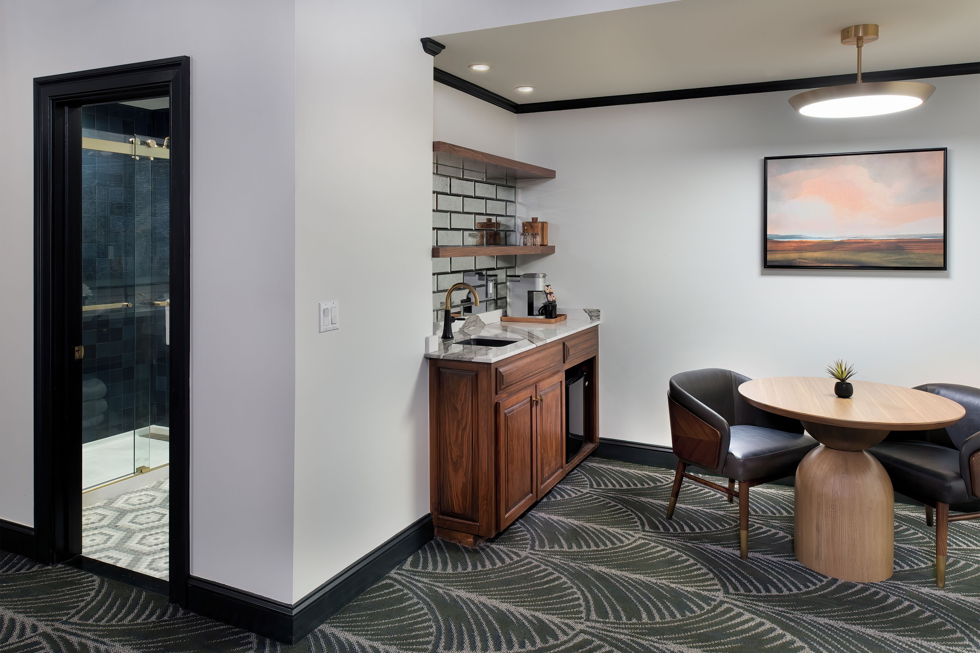 A modern kitchen with a wooden cabinet, a round table with chairs, and a painting on the wall.