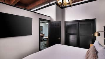 A modern hotel room with a large bed, a flat-screen TV mounted on the wall, and a dark wooden door.