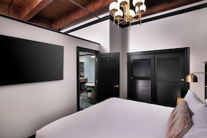 Una habitación de hotel moderna con una cama grande, un televisor de pantalla plana en la pared y una puerta de madera oscura.