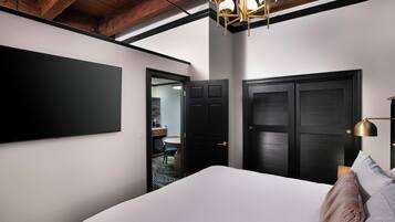 A bedroom with a large bed, a flat-screen TV mounted on the wall, and a ceiling light fixture.