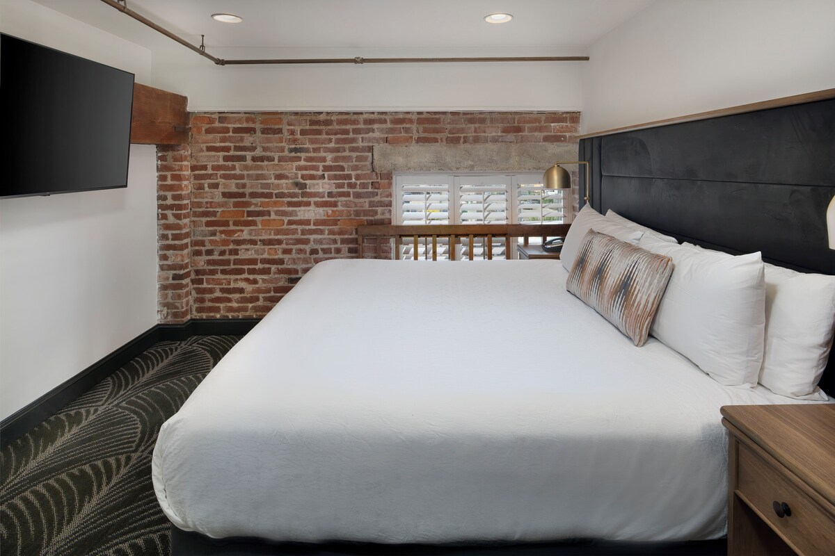 A modern bedroom with a large bed, a brick wall, and a view of a parking garage.