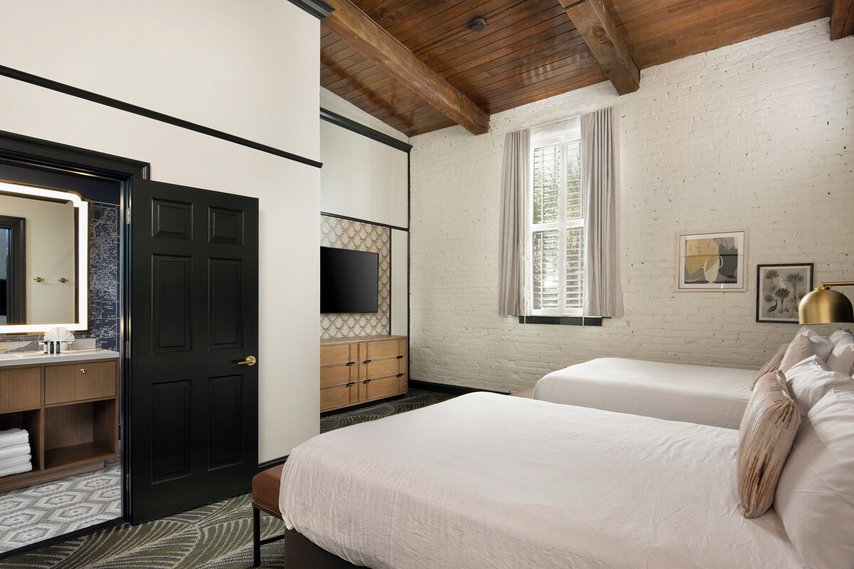 A bedroom with a wooden ceiling, a large mirror, a wardrobe, a TV, a window with curtains, and a bed with pillows.