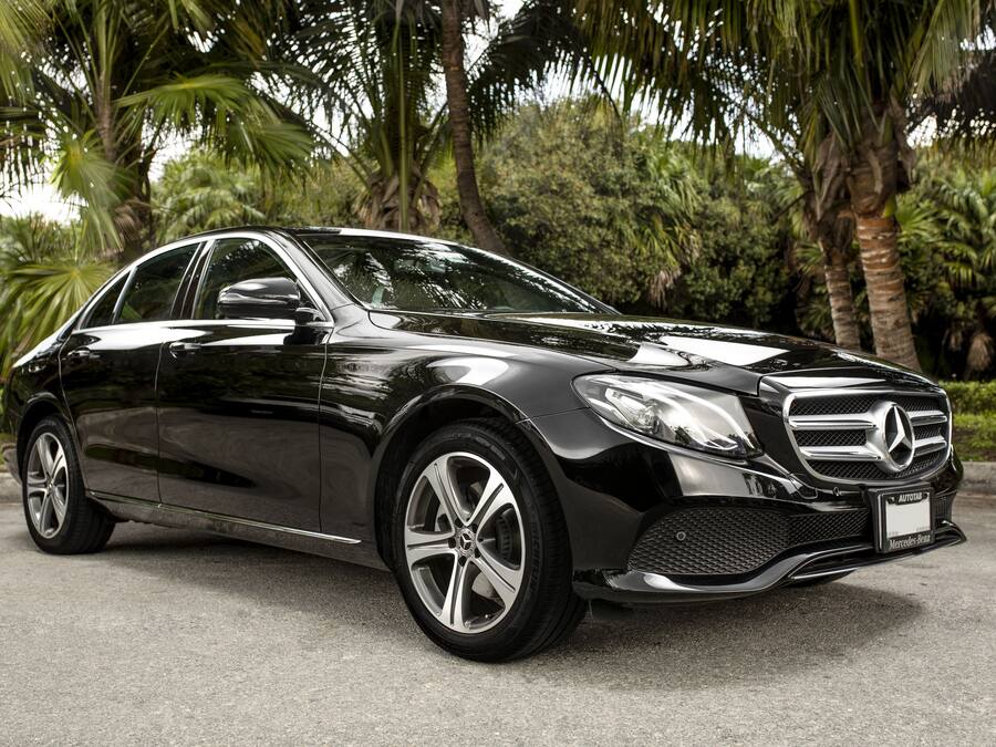 Un Mercedes-Benz negro estacionado sobre una superficie pavimentada, con palmeras al fondo.