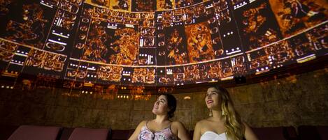 Deux personnes sont assises dans un cinéma, devant un grand écran circulaire sur lequel est projeté un film.