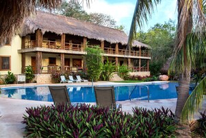Un resort con piscina, sillas de descanso y un edificio con techo de paja.
