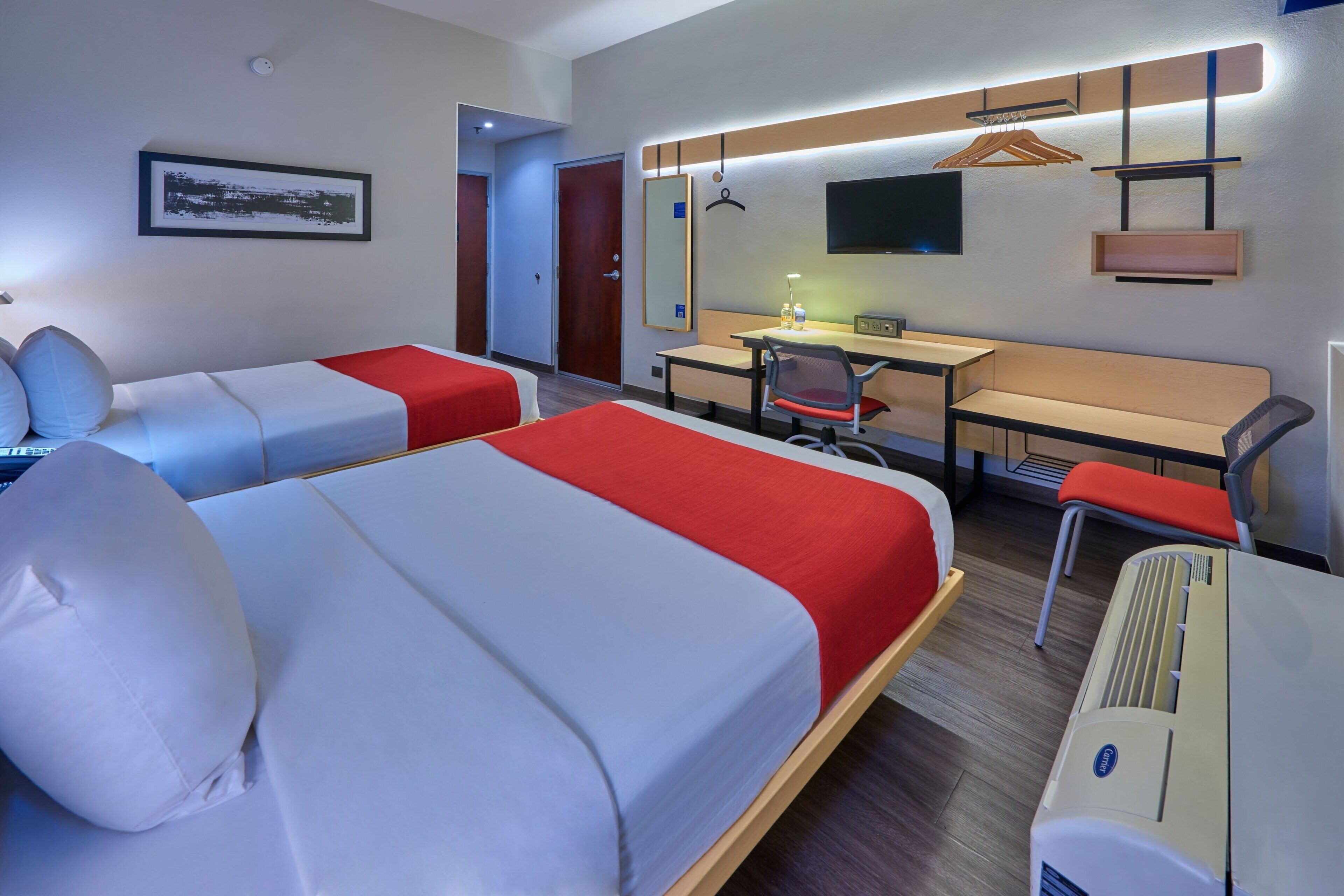 A hotel room with two beds, a desk, a chair, a TV, and a heater.