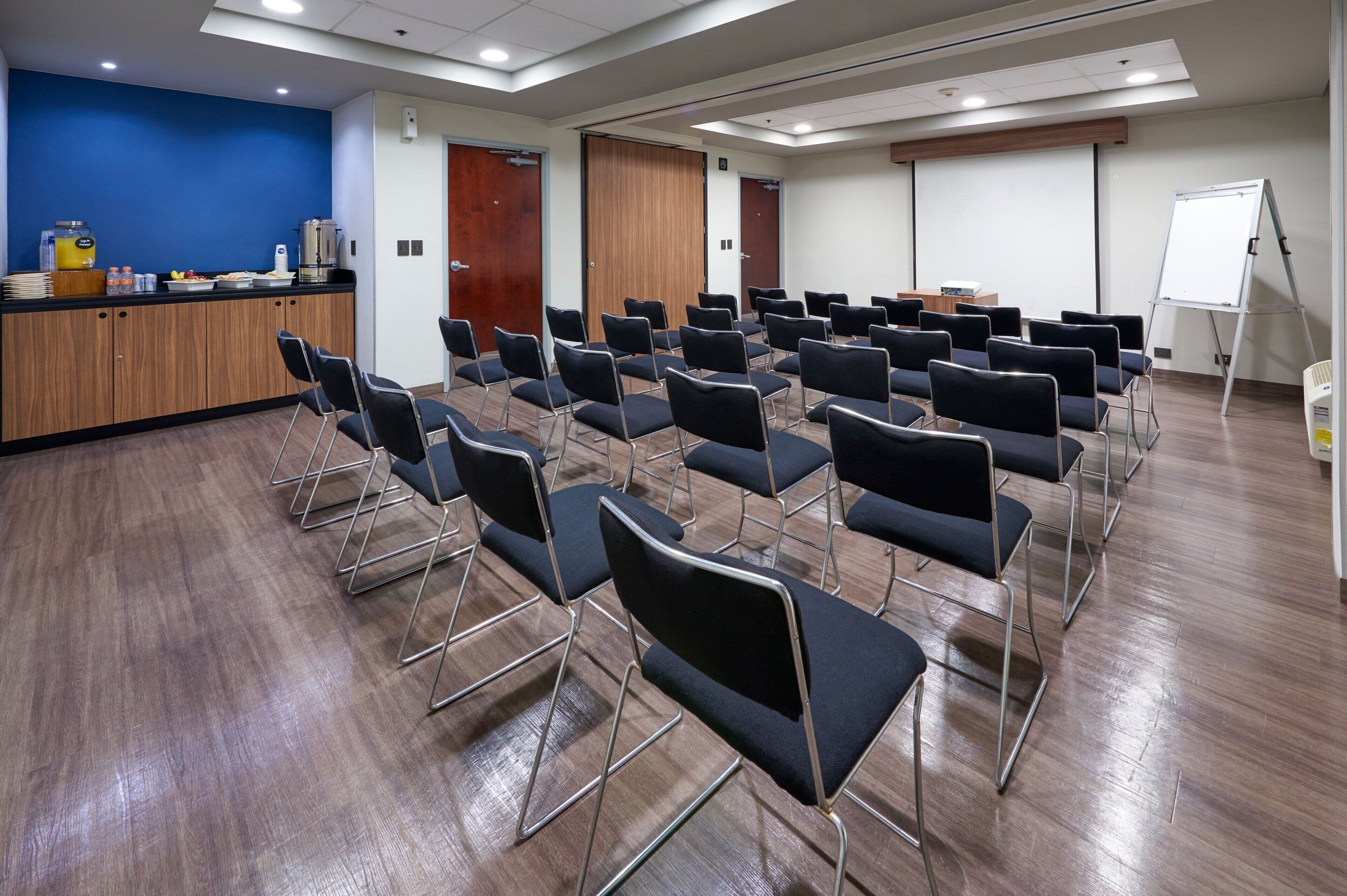 A conference room with rows of chairs, a podium, a whiteboard, and a buffet area with food and drinks.