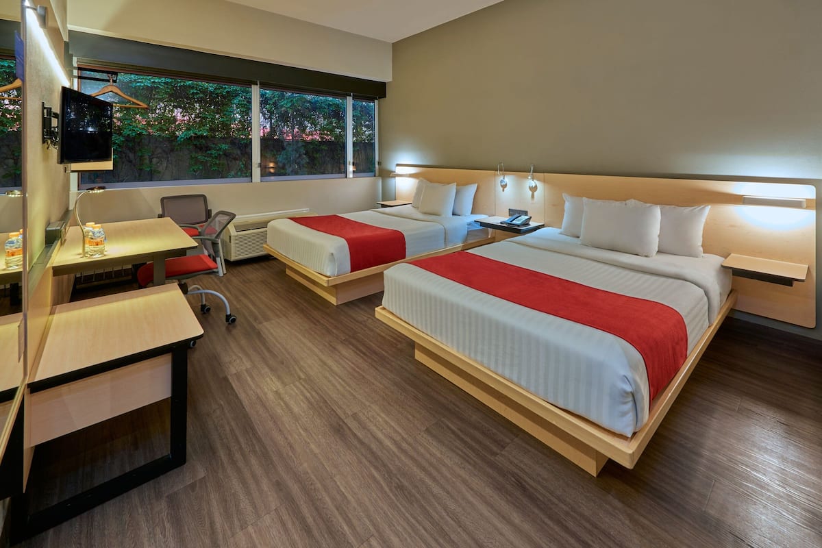 A hotel room with two beds, a desk, a chair, a TV, and a window with a view of trees.