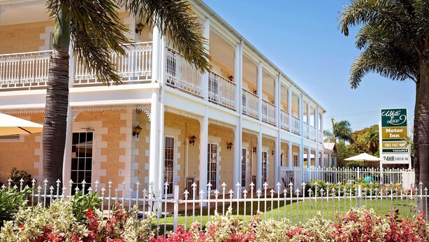 A two-story hotel with a white facade, balconies, and a sign indicating a motor inn with free fast check-in and 24-hour check-in. - White Lace Motor Inn (West Mackay)