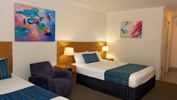 A hotel room with two beds, a chair, and artwork on the walls.