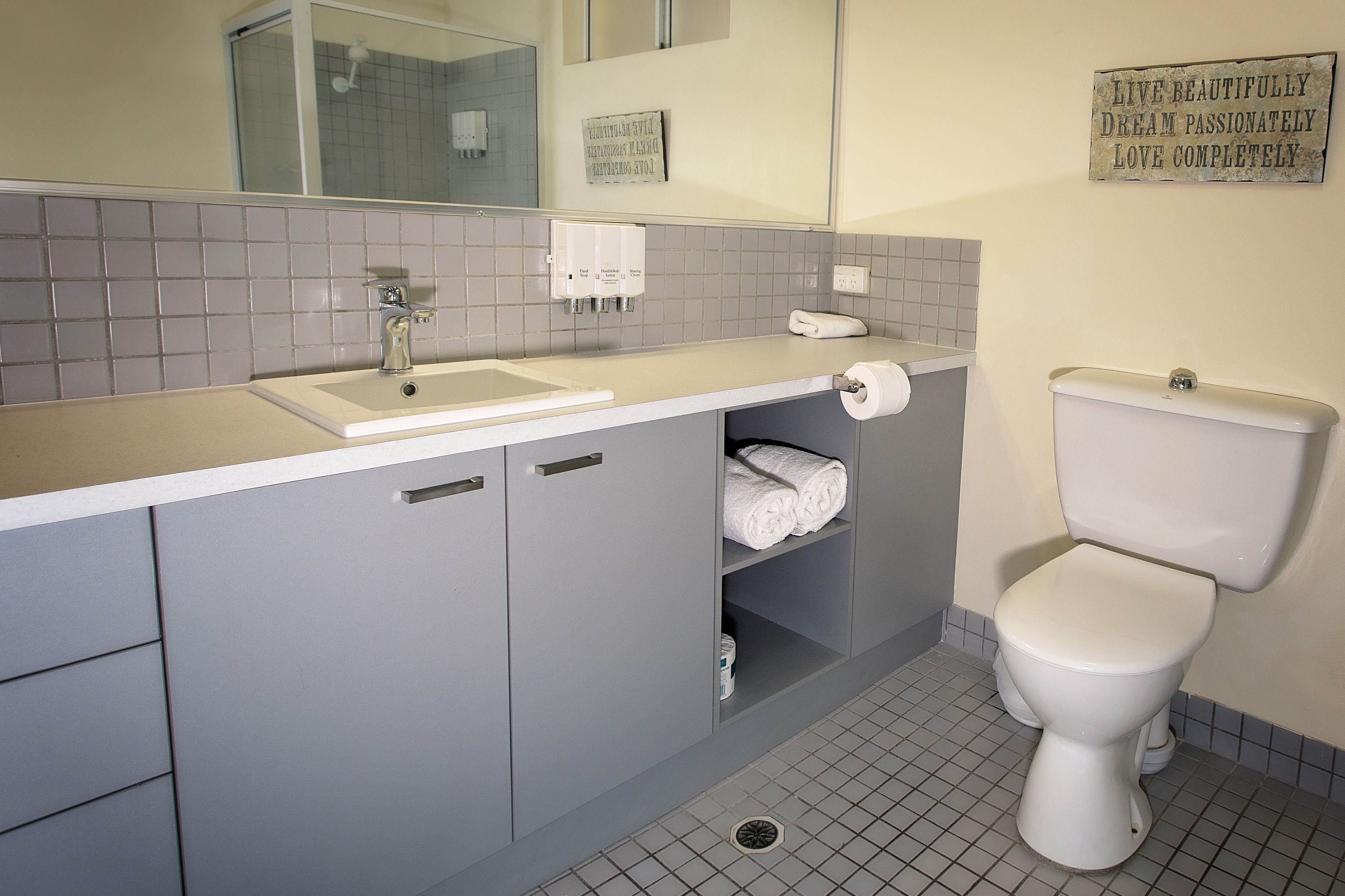 A bathroom with a white sink, grey cabinets, a toilet, and a mirror.