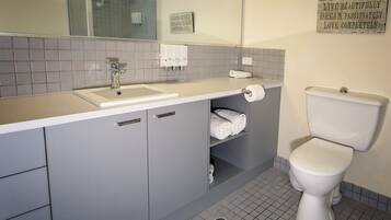 A bathroom with a white sink, grey cabinets, a toilet, and a mirror.