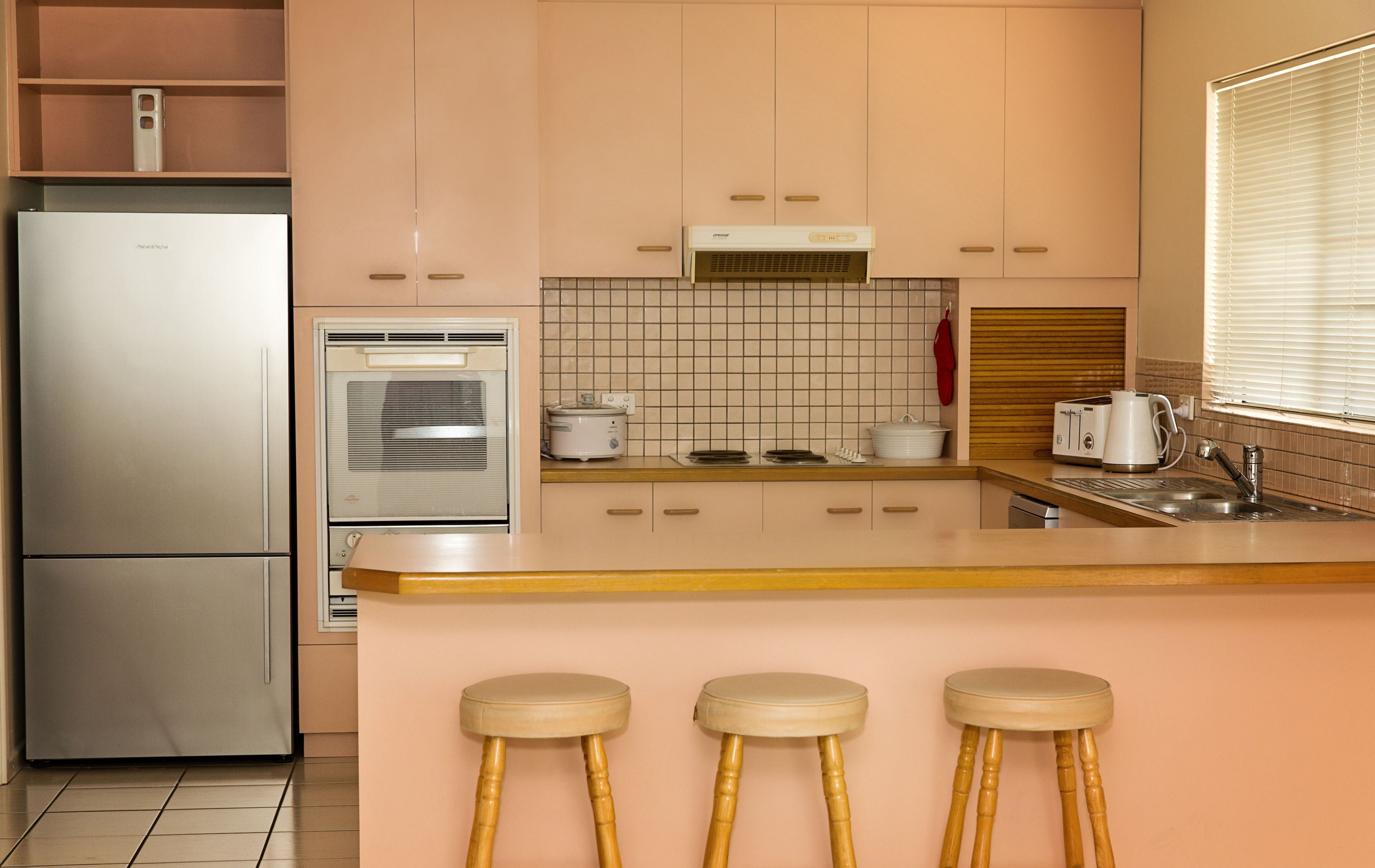 Eine Küche mit Kühlschrank, Backofen, Toaster und Holz-Barhocker.