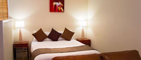 A neatly arranged hotel room with a bed, two bedside tables with lamps, a brown leather chair, and a red abstract painting on the wall.